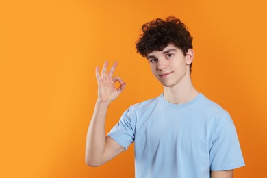 Photo of Portrait of teenage boy showing ok gesture on orange background. Space for text