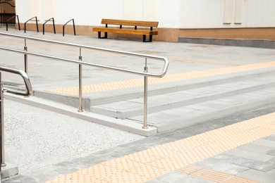 Outdoor stairs with ramp, metal railing and tactile tiles. Public environment accessibility