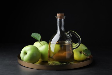 Fresh ripe green apples and jug of tasty juice on black table