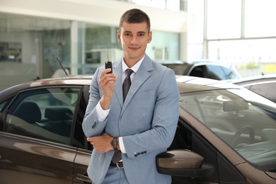 Young salesman with key near car in modern dealership