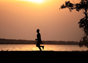 Young man running near river at sunset
