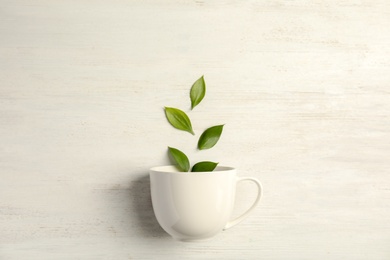 Flat lay composition with teacup and green leaves on wooden background