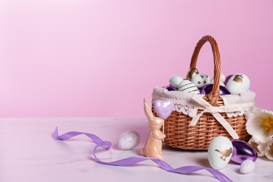 Photo of Wicker basket with festively decorated Easter eggs, bunny and beautiful tulips on white marble table against pink background. Space for text