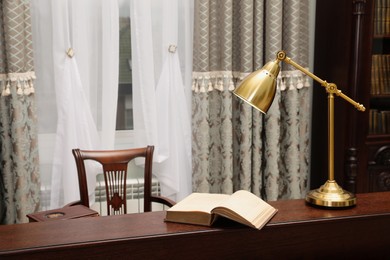 Photo of Book and lamp on wooden table in library reading room