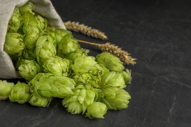 Photo of Sack with fresh green hops and spikes on black table, closeup