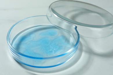 Petri dish with liquid and lid on white marble table, closeup