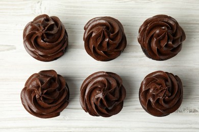 Delicious chocolate cupcakes with cream on white wooden table, flat lay