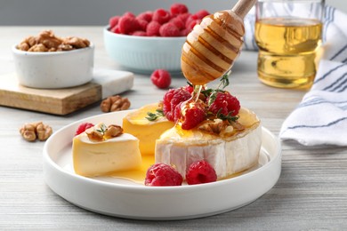 Pouring honey onto brie cheese served with raspberries and walnuts on white wooden table