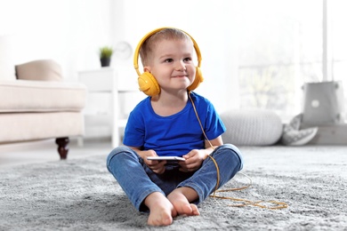 Cute child with headphones and mobile phone on floor indoors