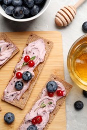 Tasty cracker sandwiches with cream cheese, blueberries, red currants, thyme and honey on grey marble table, flat lay