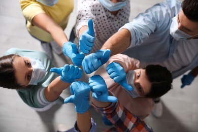 Group of people in blue medical gloves showing thumbs up indoors, top view