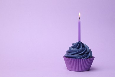 Photo of Delicious birthday cupcake with dark blue cream and burning candle on violet background. Space for text