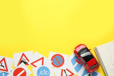 Many different road sign cards, notebook and toy car on yellow background, flat lay with space for text. Driving school