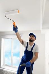 Photo of Handyman painting ceiling with white dye indoors