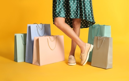 Young woman with paper shopping bags on yellow background, closeup