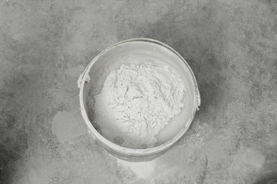 Bucket with powdered plaster and liquid on concrete floor, top view