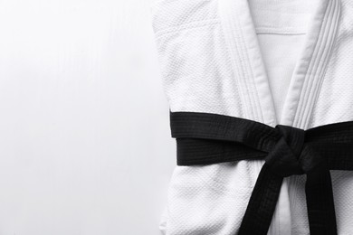 Martial arts uniform with black belt on white wooden background, top view. Space for text