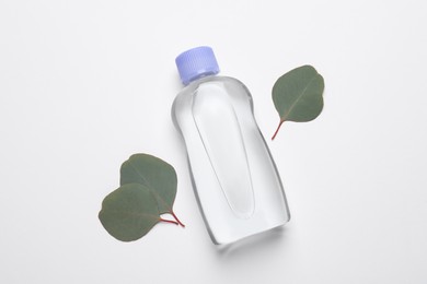 Bottle of baby oil and eucalyptus leaves on white background, flat lay