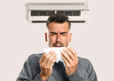 Man suffering from cold in room with air conditioner on white wall