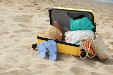 Open suitcase with beach items on sandy coast