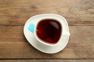 Tea bag in ceramic cup of hot water on wooden table, top view