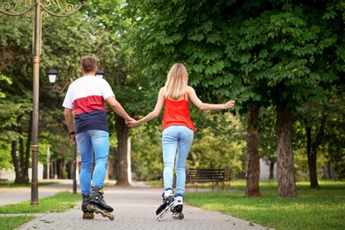 Photo of Young couple roller skating in summer park, back view