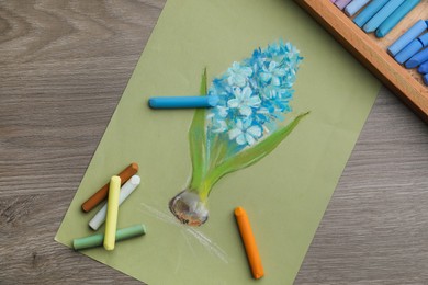 Beautiful drawing of blooming hyacinth and pastels on wooden table, top view