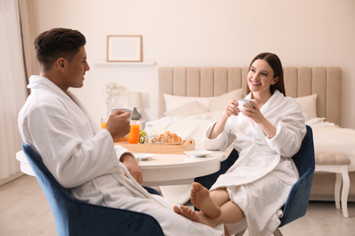 Happy couple in bathrobes having breakfast at home
