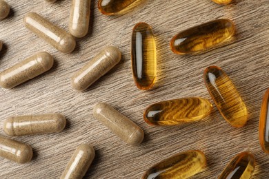 Photo of Different dietary supplements capsules on wooden table, flat lay