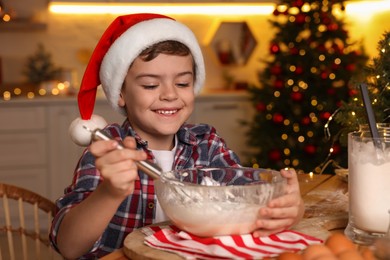 Cute little boy in Santa hat making dough for Christmas cookies at home