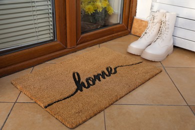 Photo of Doormat with word Home and stylish boots near entrance outdoors