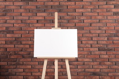 Wooden easel with blank canvas near brick wall