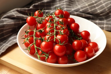 Plate of ripe whole cherry tomatoes on wooden table, closeup