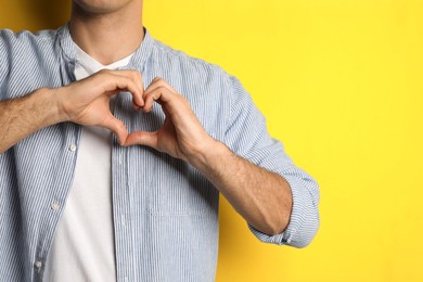 Man making heart with hands on yellow background, closeup. Space for text