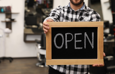 Young business owner holding OPEN sign in his barber shop, closeup
