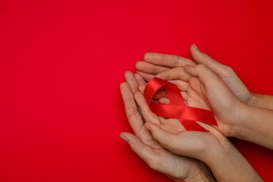 Woman and girl holding red ribbon on bright background, top view with space for text. AIDS disease awareness