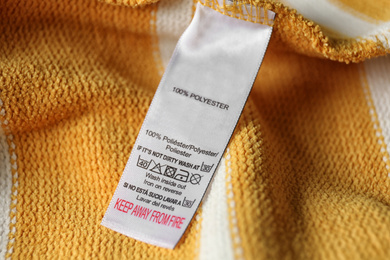 Clothing label with care symbols and material content on yellow shirt, closeup view
