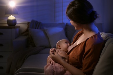 Young woman breastfeeding her little baby indoors at night, space for text