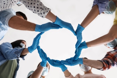 People in blue medical gloves showing circle with hands on light background, low angle view