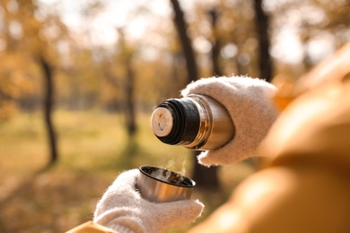 Woman pouring drink from thermos into cap outdoors, closeup. Space for text