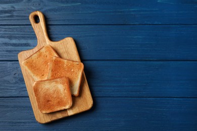 Board with slices of delicious toasted bread on blue wooden table, top view. Space for text