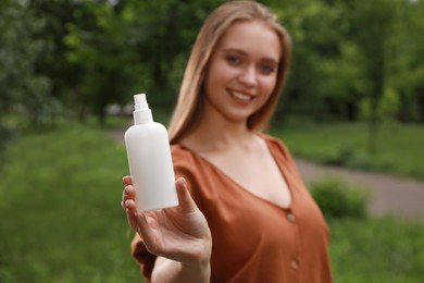 Woman with insect repellent spray in park, focus on bottle. Tick bites prevention