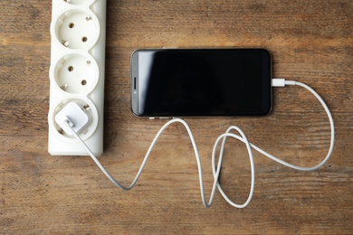 Photo of Smartphone charging with cable on wooden table, flat lay
