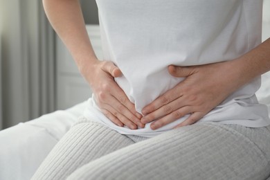 Woman suffering from abdominal pain on bed at home, closeup