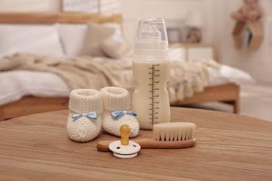 Baby booties, pacifier, feeding bottle and brush on wooden table in bedroom. Maternity leave concept