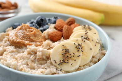 Tasty oatmeal porridge with toppings in bowl on table, closeup