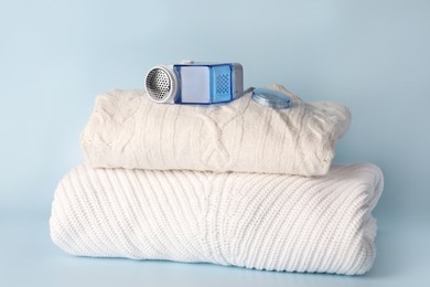Photo of Modern fabric shaver and knitted clothes on light blue background