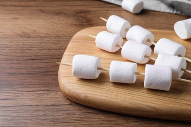 Sticks with delicious puffy marshmallows on wooden table. Space for text
