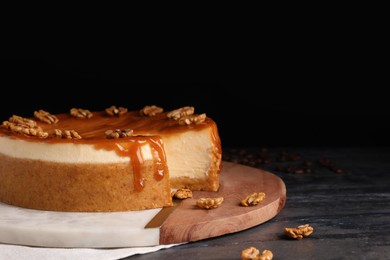 Delicious cheesecake with caramel and walnuts on black marble table, space for text