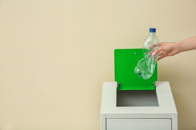 Woman throwing empty plastic bottle into trash bin on color background, closeup with space for text. Recycling concept